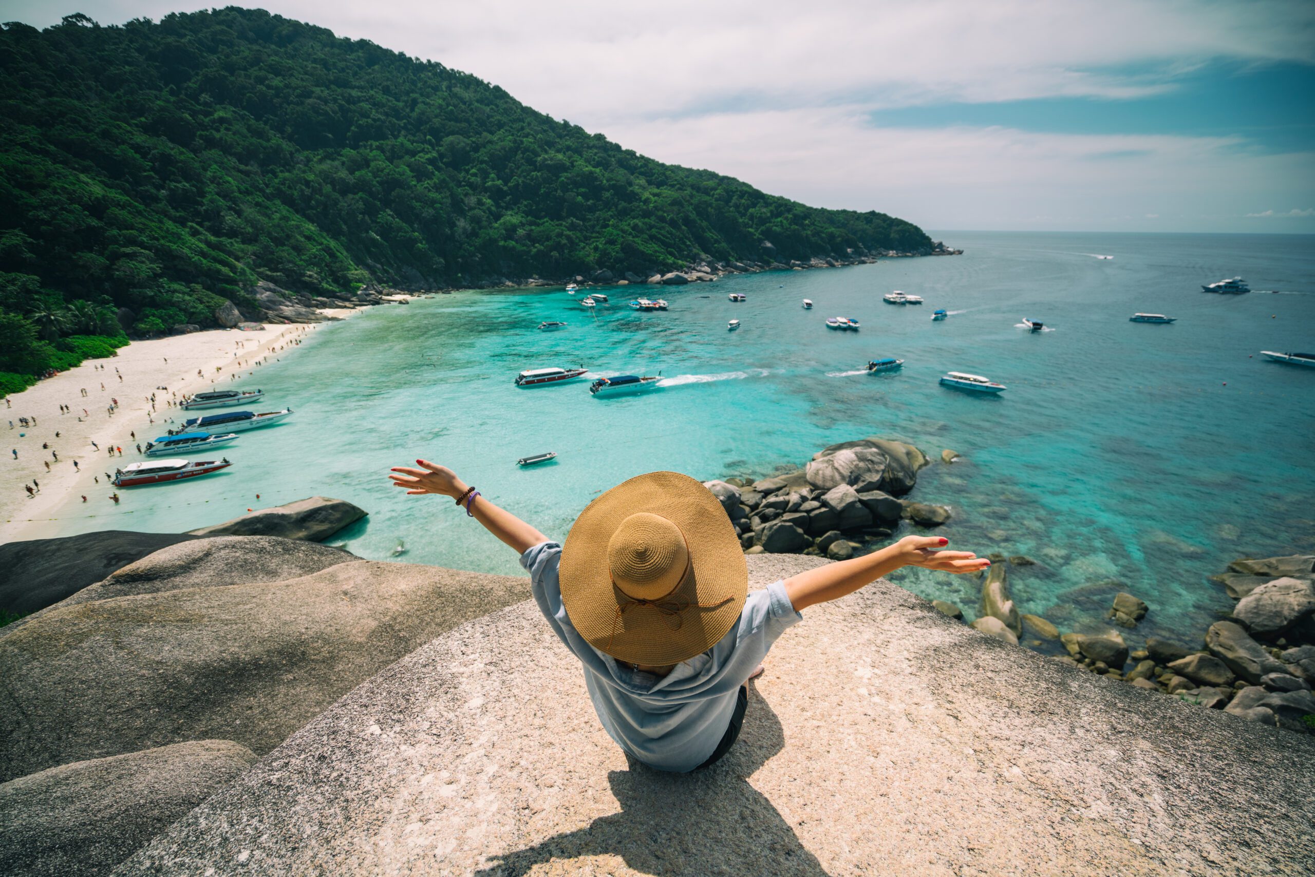 Rear view of young woman traveler with hat sitting and relaxing on viewpoint at similan islands in Andaman sea at Phang Nga province near Phuket and Krabi in southern of Thailand. Summer Relax